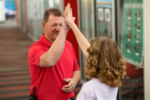 Staff member in red polo tshirt high fiving a female middle school student in the hallway